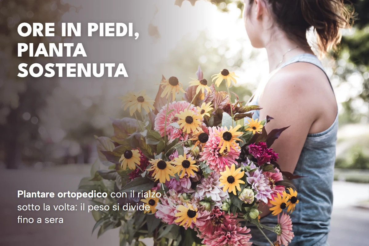 Donna di spalle con un grande mazzo di fiori in mano, in piedi in una via alberata